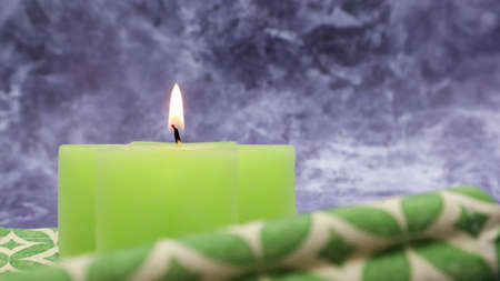 Composition with one green lit candle on a table with a green linen napkin against a beautiful gray marble background. Place for your text. Christmas decorations.の写真素材