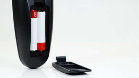 Black TV remote control with AAA alkaline batteries in red and white on a white background. Battery...