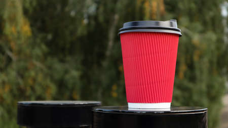 Coffee in a paper disposable eco glass of red color with a black plastic lid against the background...