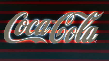 View of a glowing white Coca-Cola sign in the dark. Coca Cola sign. Non-alcoholic carbonated drink....