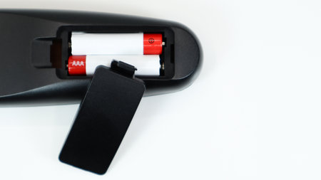 Black TV remote control with AAA alkaline batteries in red and white on a white background. Battery...