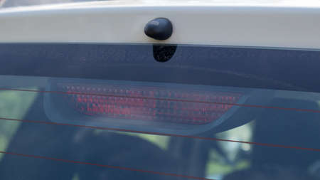 Rear window of a dusty white car with a stoplight behind glass, close-up. Red signals indicating vehicle braking. They turn on automatically when you press the brake and turn off when you release itの写真素材