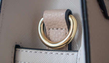 Metal gold loop oval ring attached to a leather bag. Selective focus. Part for a secure connection between two objects. Sewing accessories in the form of a ring for sewing bags, glossyの写真素材