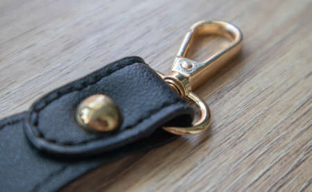Swivel carabiner fastener with leather black bag strap on a wooden background. Metal carabiner with swivel clip or hook. Small gold fittings close-up in selective focusの写真素材