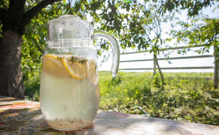 Homemade lemonade made from lemons in a large glass jug on the table in the garden. A jug with lemon...