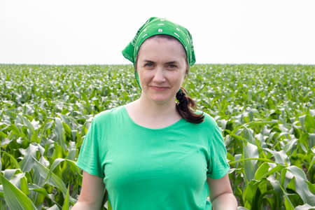 Beautiful smiling young woman farmer in green t-shirt and green sun hat standing in the middle of a...