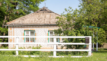 Summer old brick house in the village. View of a traditional village house in the countryside behind a white board fence and trees on a sunny summer dayの写真素材
