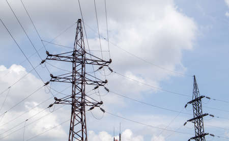 High voltage electrical tower. Power lines and power pylons on a sunny day with circular clouds in...