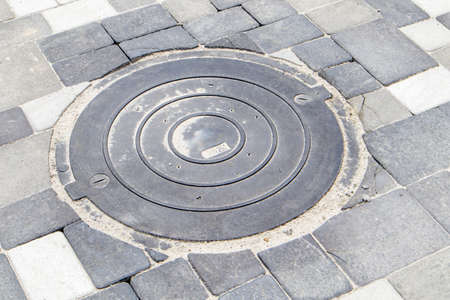 New plastic manhole cover on the sidewalk lined with gray paving slabs. The concept of sewerage,...