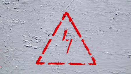 Red electrical hazard sign with lightning in a triangle on a gray painted metal junction boxの写真素材