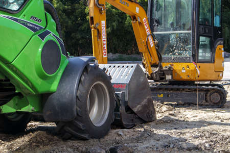Two small excavators on a large construction site. Bright green on wheels and yellow on tracks. Earthworks and construction. Shovel excavator. Mini loaders. Ukraine, Kiev - August 28, 2021のeditorial素材