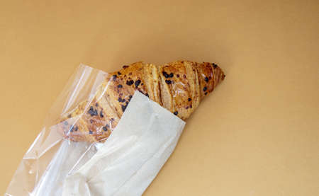 One regular fresh crispy whole grain croissant with chocolate filling on a brown or coffee background with copy space. Classic traditional freshly baked French dessert, pastries. Top view, flat layの写真素材