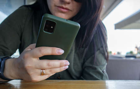 Close up of woman's hand with wedding ring holding cell or mobile phone during coffee break. A woman...