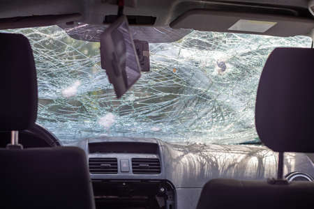 Broken windshield of a car from a bullet, from a shot from a firearm, view from the inside of the cabin. Damaged glass with traces of an oncoming stone on the road.の写真素材