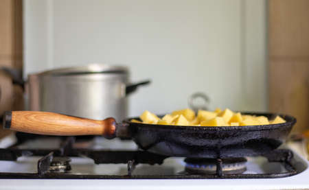 Roasting fresh potatoes in a cast iron skillet with sunflower oil. A view of a stovetop with a frying pan filled with golden fried potatoes in a real kitchen. food cookedの写真素材