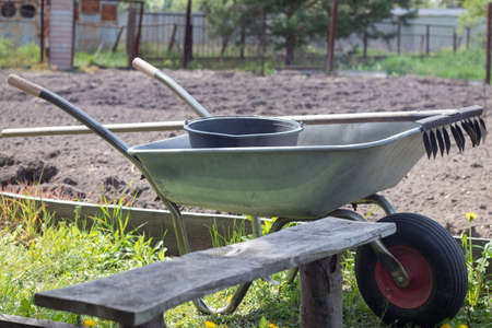 Gray metal garden wheelbarrow with two handles and one wheel. The wheelbarrow is in the garden or...