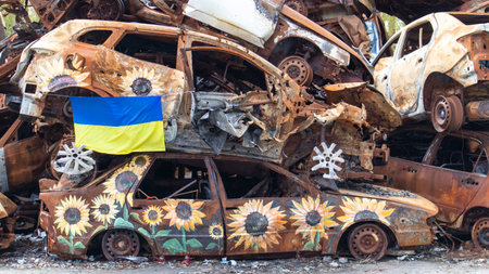 The national flag of Ukraine against the background of ruins and rusty metal of destroyed cars. A blue-yellow flag waving in the wind under the sun. Ukraine, Kyiv - April 29, 2023のeditorial素材