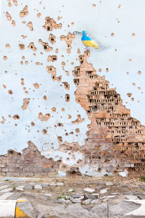 Shelled wall with a drawing of a dove in the colors of the flag of ukraine, blue and yellow. The dove is a symbol of purity, light, peace, love, the human soul. Ukraine, Kyiv - May 06, 2023.のeditorial素材