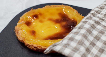 One freshly baked Pastel de nata or Portuguese egg tart in a baking dish. Pastel de Belm is a small...