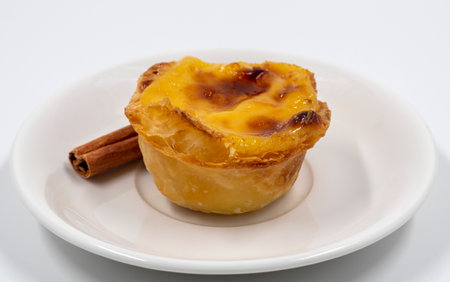 Plate with one Portuguese Pastel de Nata pie with custard and cinnamon sticks. Pastel de Belem is an...
