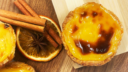 Pastel de nata tarts or Portuguese egg tart and cinnamon sticks on a wooden brown background. Pastel...