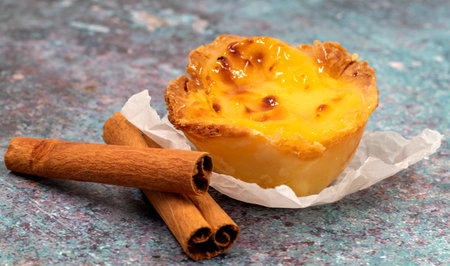 One Pastel de nata or Portuguese egg tart and cinnamon sticks. Pastel de Belm is a small pie with a...