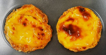 Two freshly baked Pastel de nata or Portuguese egg tart desserts in a baking dish. Pastel de Belm is...