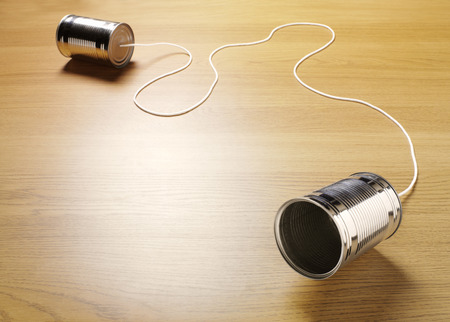 Two tin cans joined with a cord on a wooden background for primitive communicationの写真素材