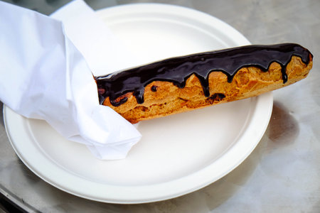 A single chocolate eclair on a white plate