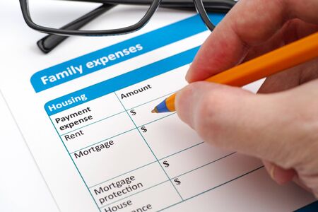 Family expenses applicacion form, glasses and human hand with ballpoint pen.