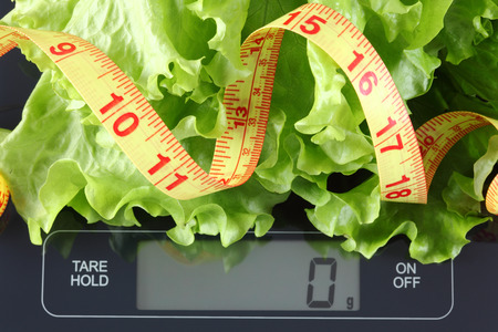 Green lettuce and tape measure in a black plate on digital scale displaying 0 gram.の写真素材