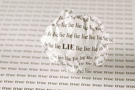 Crumpled paper ball with words "Lie" on background with words "true". Sepia.の写真素材