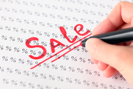 Woman's hand with red pen writing word "Sale" on the background of percentage signs.の写真素材