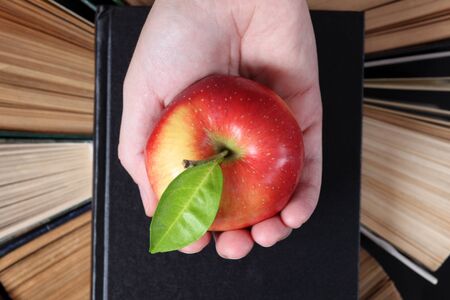 Woman's hand with apple above old hardback books.の写真素材