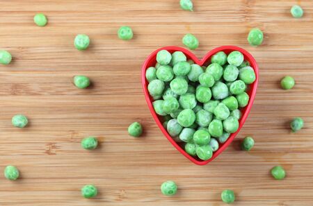Fresh frozen green peas in a heart bowl. Close-up.の写真素材