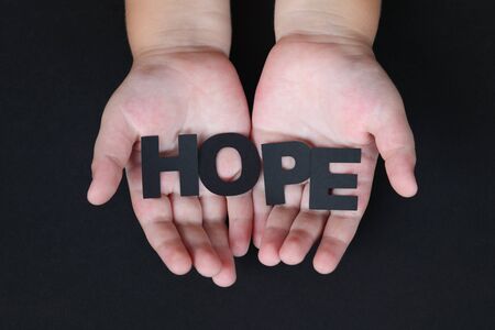 Word \"Hope\" in children\'s hands on black . Letters is made of black paper.の写真素材