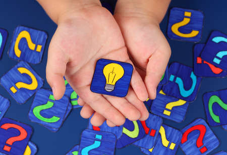 Yellow light bulb in child\'s hands on blue with a lot of question marks. Pictures drawn by me.の写真素材