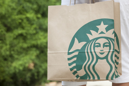 Paphos, Cyprus - November, 23 2013 Woman standing on the street with Starbucks takeaway paper bag in her hands. Urban scene. Starbucks Corporation is the largest coffeehouse company in the world based in Seattle, Washington.のeditorial素材