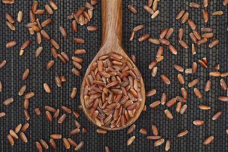 Red rice in a wooden spoon on black napkin.の写真素材