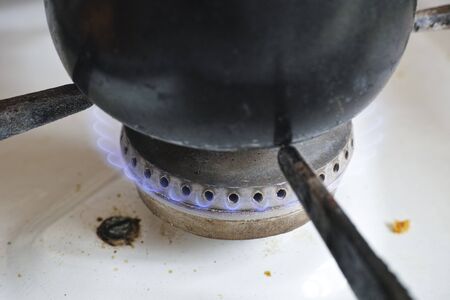 Pot on flame burning of old dirty gas cooker .