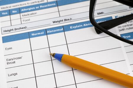 Page of Health History form with pre-participation physical information. There are glasses and ballpoint pen on page.の写真素材