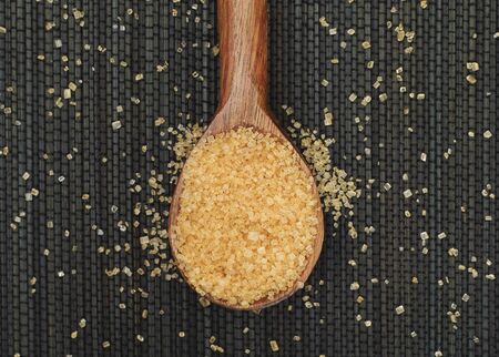 Brown cane sugar crystals in a wooden spoon on black napkin. Adobe RGB.