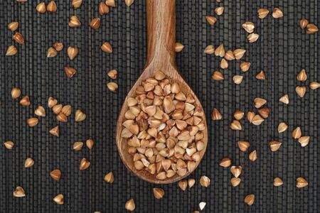 Buckwheat in wooden spoon on black napkin.