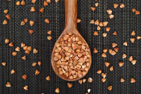Buckwheat in wooden spoon on black napkin.