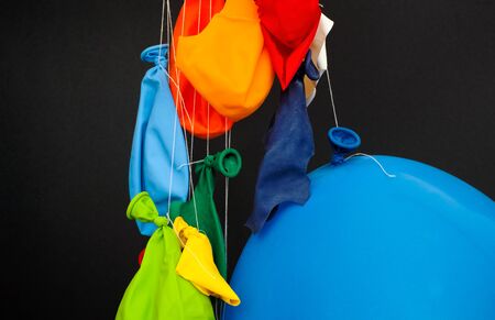 End of the party. Some burst, deflated balloons and one inflated balloon hanging on threads on black background.の写真素材