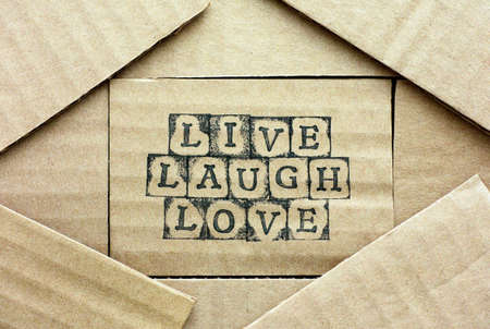 Cardboard card with words Live Laugh Love made by black alphabet stamps with piece of cardboard. 