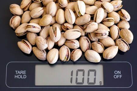 Roasted and salted pistachios on digital scale displaying 100 gram.