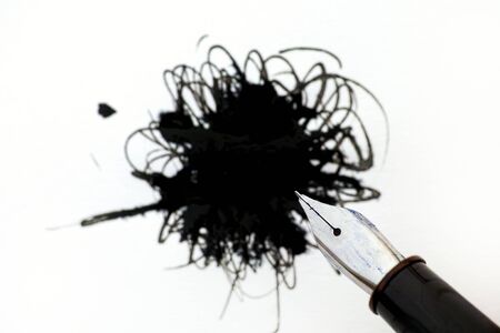Ink pen against black ink spot on white paper. Focus on pen.の写真素材
