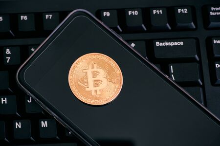 Golden Bitcoin virtual money on mobile phone on keyboard. Close-up.の写真素材