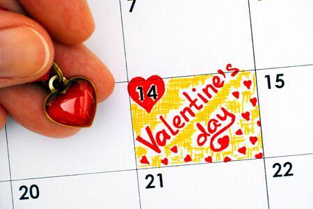 Reminder Valentine`s Day in calendar and person hand with red heart. Close-up.